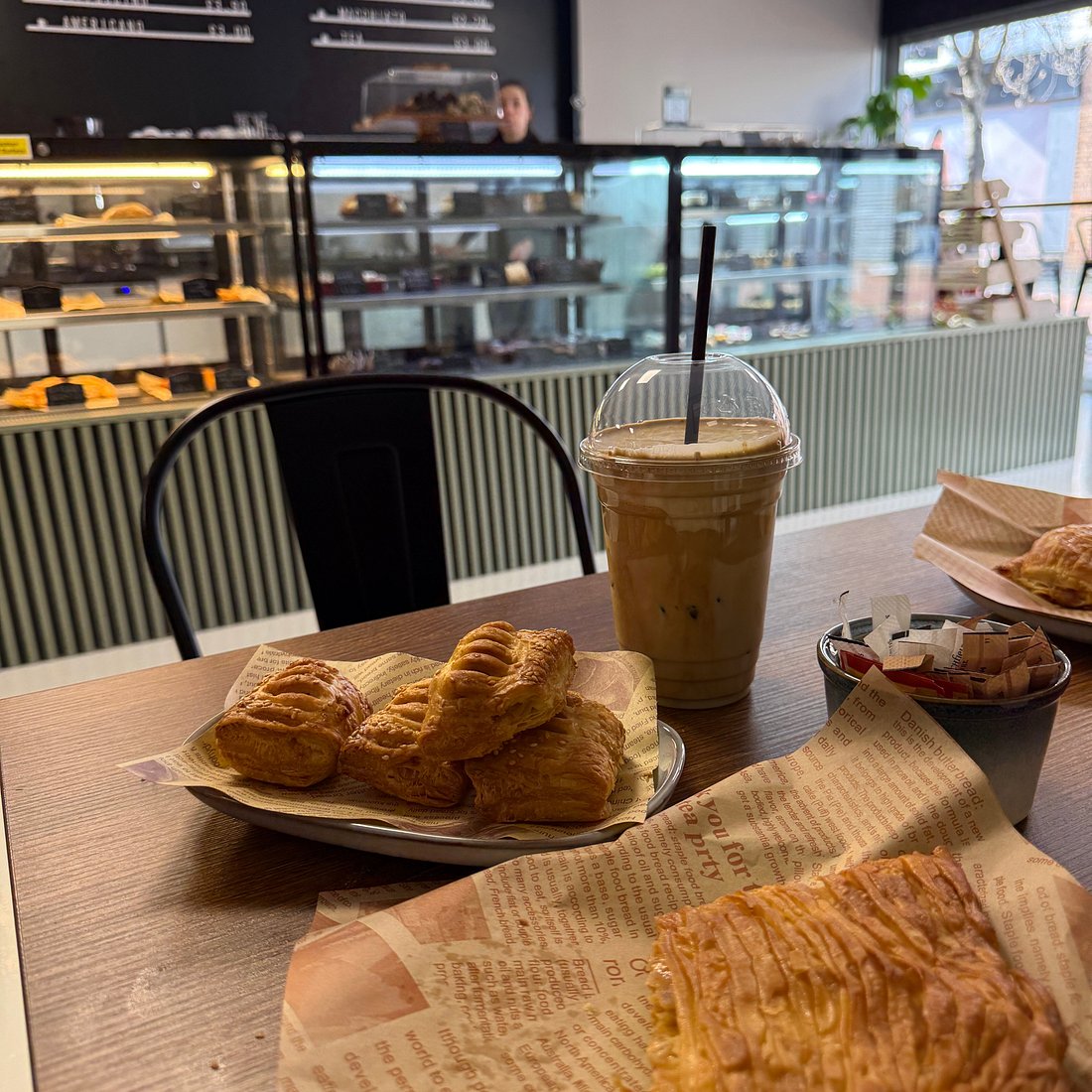 Pastries and a drink on a table with The Greek Spot counter behind
